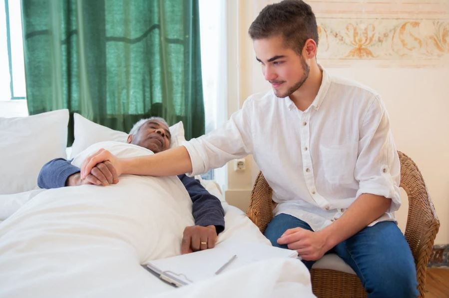 a man in a white button up shirt sitting beside an elderly man in bed