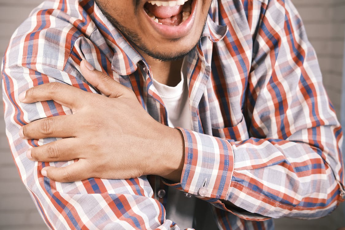 close-up photo of an aching man holding his shoulder