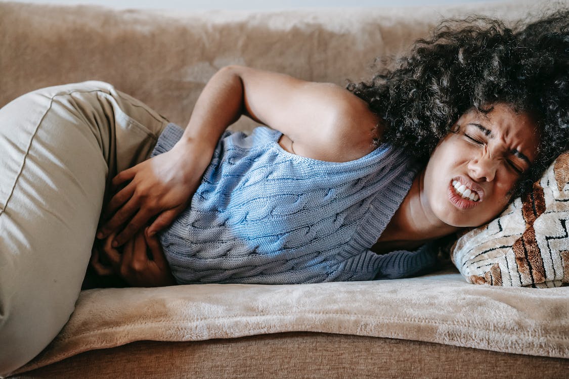 woman suffering from stomach pain lying down on a couch