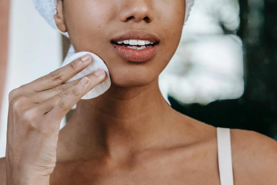 crop ethnic woman cleaning the face with a cotton pad