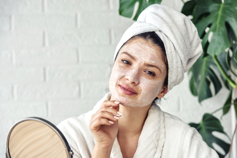 Young woman cleaning face with natural cosmetics. How to get clear and glowing skin. Portrait of young woman with clay face mask on wearing bathrobe. Homemade Face Mask