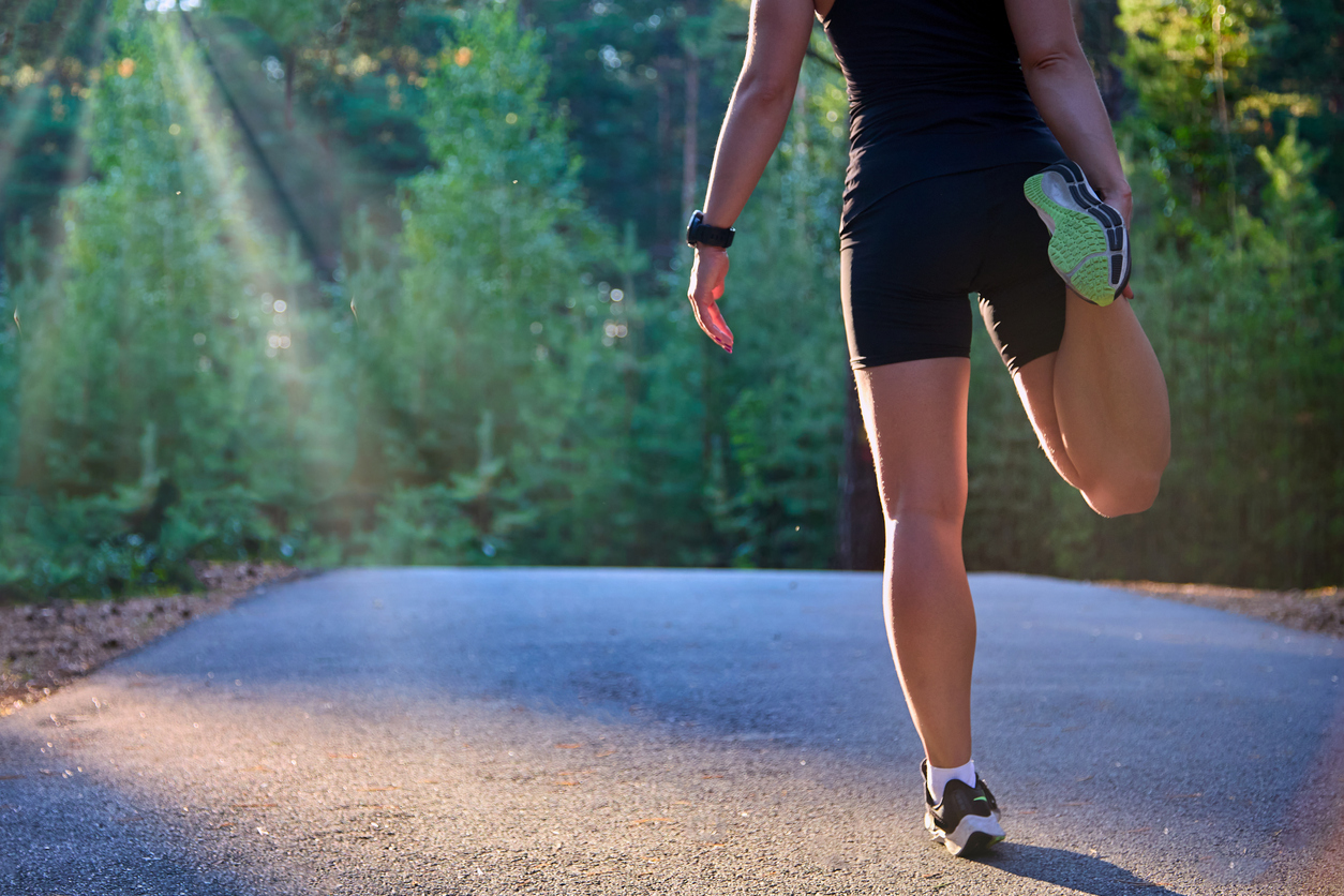Athlete-runner stretching her legs and feet and preparing to run on an asphalt road in the forest