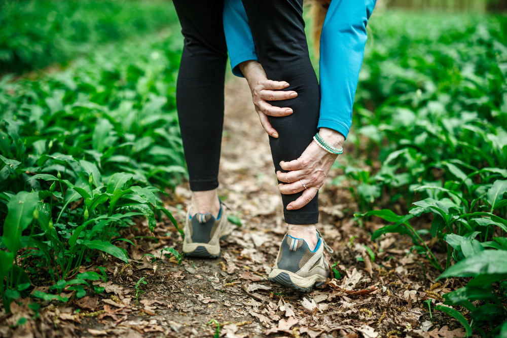 Woman touching her calf on footpath, suffering from leg pain or cramp during a hike