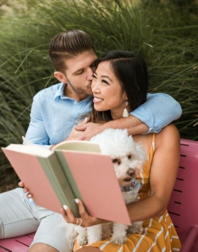 A man kissing a woman holding her book and a dog