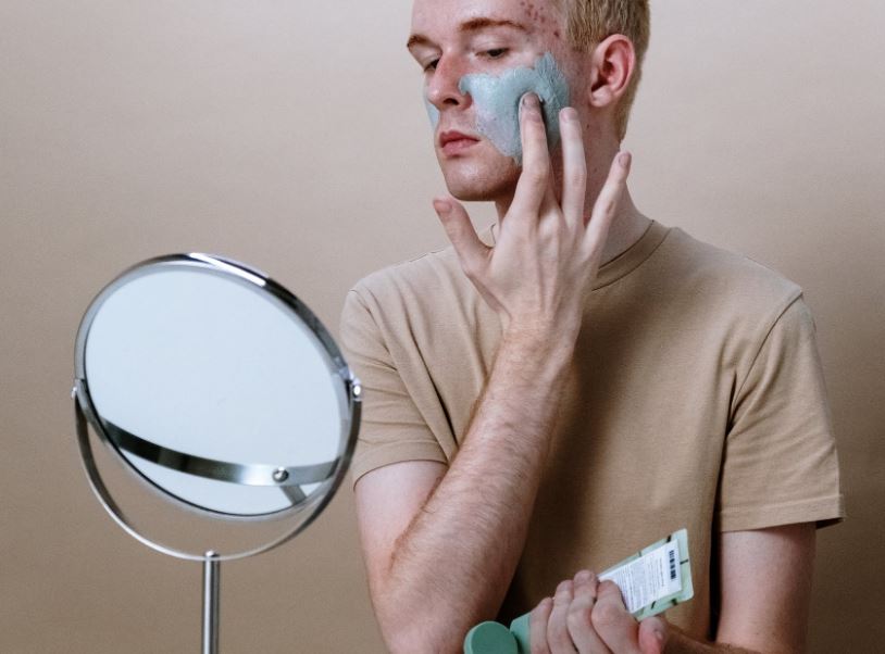 a man looking at a mirror as he applies a cream for his acne scars